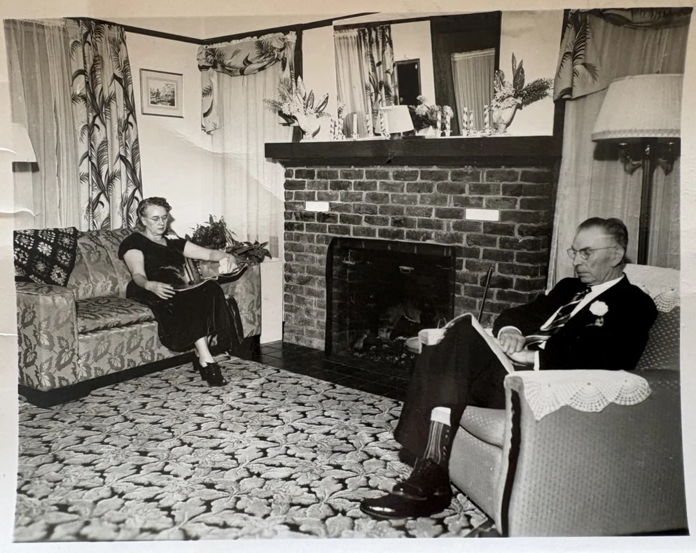 Historic family photograph showing two people seated beside the living-room fireplace