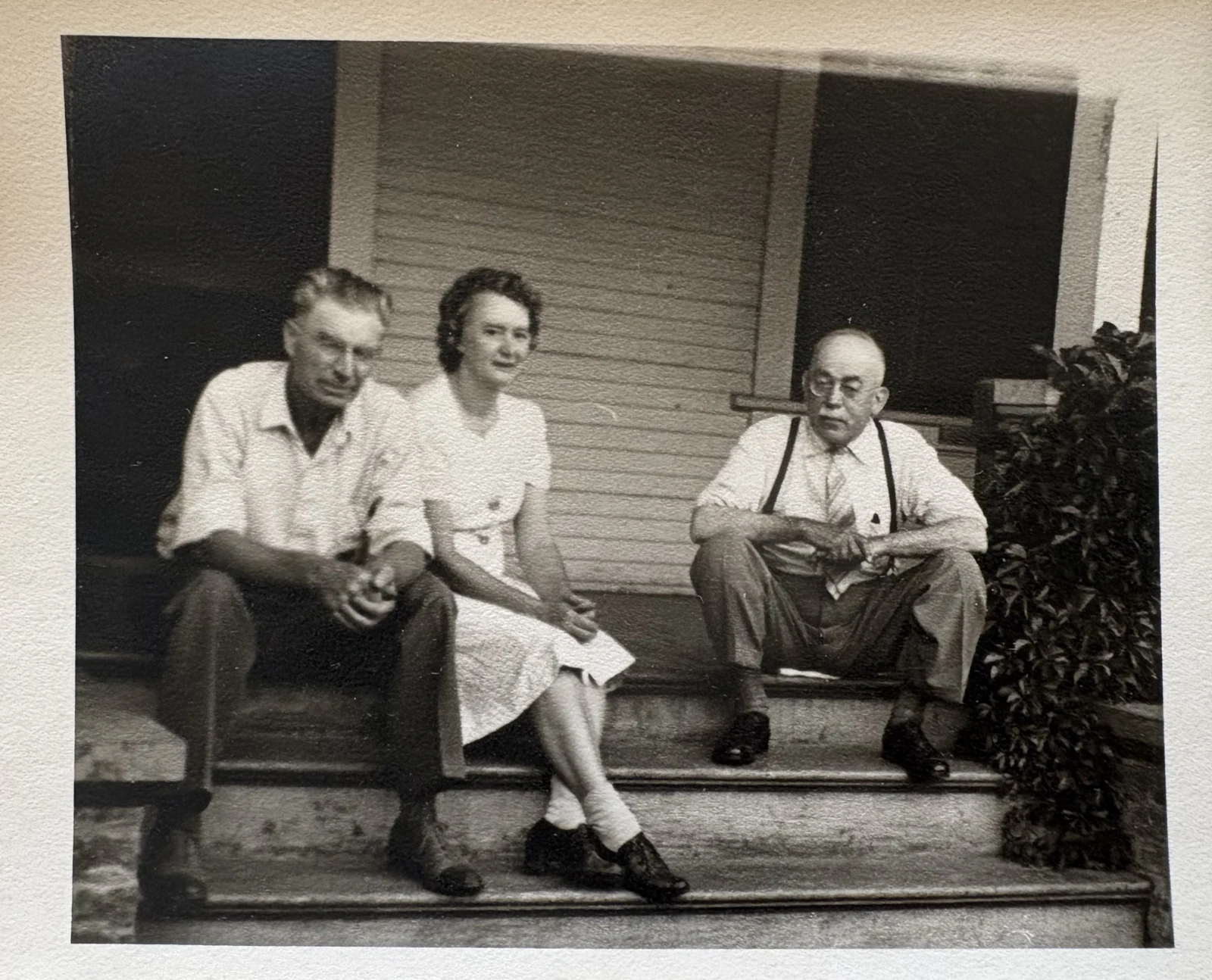 Historic family photograph showing three people sitting on the front steps